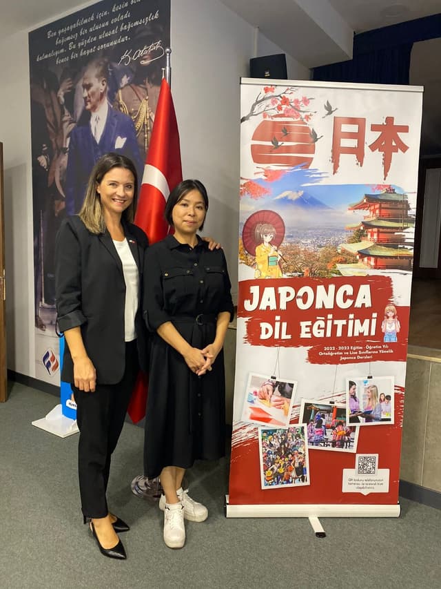 Two women posing next to the Japanese language education banner at Final Schools