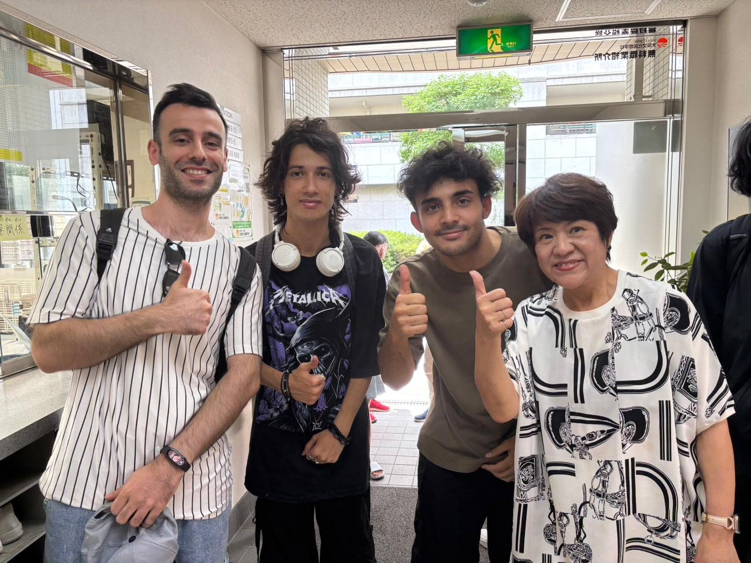 Three students and a Japanese woman giving thumbs up at a school entrance in Osaka