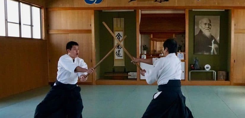 Two people practicing aikido with wooden swords in a dojo in Japan