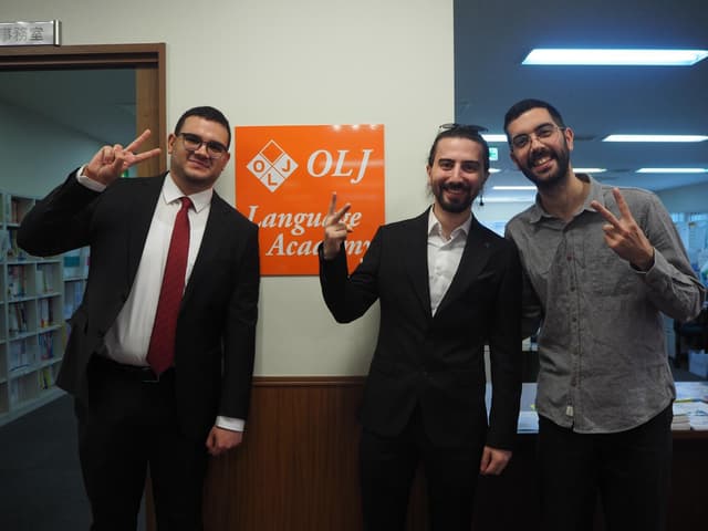 Three students making peace signs in front of the OLJ Language Academy sign