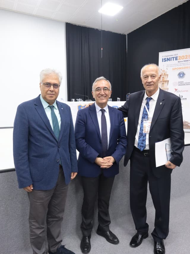 Three academics posing beside the ISNITE 2025 sponsors board